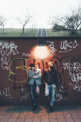 Portrait of two cool young male hipsters leaning against graffiti wall - CUF12051