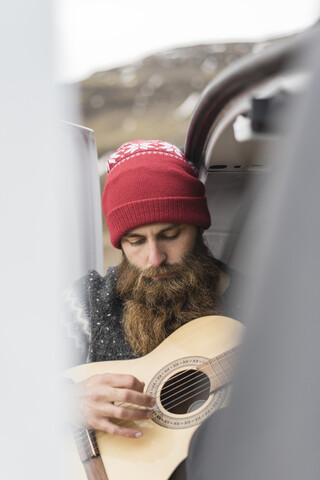 Porträt eines Hipsters mit roter Wollmütze, der Gitarre spielt, lizenzfreies Stockfoto