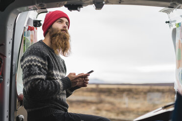 Porträt eines nachdenklichen Hipsters, der mit seinem Handy am Lieferwagen steht - AFVF00510