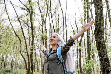 Mature woman with long grey hair with open arms in forest, Scandicci, Tuscany, Italy - CUF12085