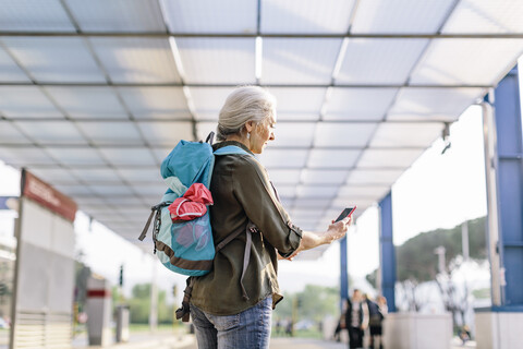 Ältere weibliche Rucksacktouristin schaut auf ihr Smartphone am Busbahnhof, Scandicci, Toskana, Italien, lizenzfreies Stockfoto