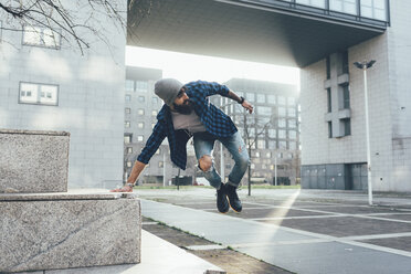 Junger männlicher Hipster springt mitten in der Luft und übt Parkour in der Stadt - CUF12193