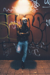 Portrait of cool young male hipster leaning against graffiti wall at night - CUF12197