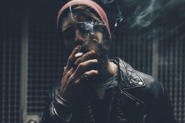 Young male hipster smoking cigarette in dark city doorway at night - CUF12202