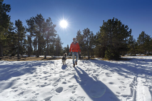 Älterer Mann geht mit Hund in verschneitem Wald spazieren - CUF12205