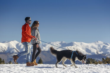 Ehepaar geht mit Hund in verschneiter Berglandschaft spazieren - CUF12207