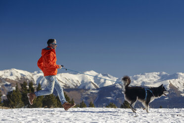 Mann läuft mit Hund in schneebedeckter Berglandschaft - CUF12208