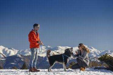 Pärchen streichelt Hund in verschneiter Berglandschaft - CUF12209