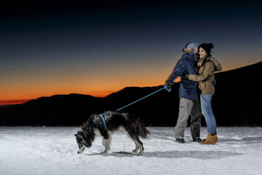 Romantisches Paar mit Hund im Schnee bei Nacht - CUF12216