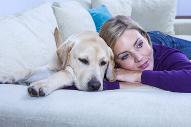 Mittlere erwachsene Frau auf dem Sofa liegend mit ihrem Labradorhund - CUF12222