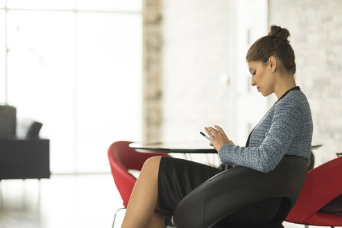 Geschäftsfrau sitzt im Büro und schaut auf ihr Smartphone - CUF12287