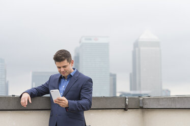 Geschäftsmann, der auf der Dachterrasse eines städtischen Büros auf sein Smartphone schaut, London, UK - CUF12311