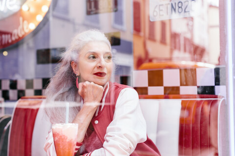 Ältere Frau in Baseballjacke schaut durch das Fenster eines Diners aus den 1950er Jahren, lizenzfreies Stockfoto