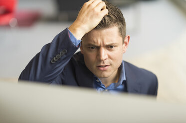 Geschäftsmann schaut auf Computer im Büro und kratzt sich am Kopf - CUF12350