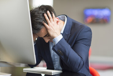 Stressed businessman at office computer with head in hands - CUF12353