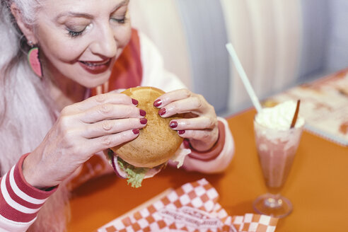 Mature woman eating burger in 1950's diner - CUF12359