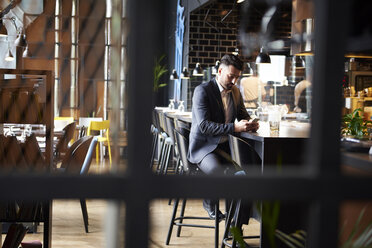 Disappointed man looking at smartphone while sitting at bar - CUF12360