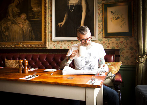Schrulliger Mann, der in einer Bar und einem Restaurant Zeitung liest, Bournemouth, England, lizenzfreies Stockfoto