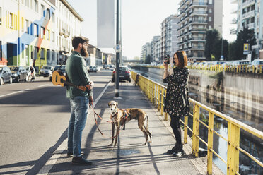 Junge Frau fotografiert Freund und Hund am Kanal mit Sofortbildkamera - CUF12410