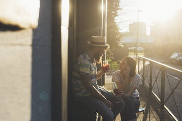 Paar sitzt vor einem sonnenbeschienenen Straßencafé und trinkt Cocktails - CUF12419