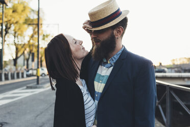 Young woman pulling boyfriend's bowler hat by city canal - CUF12426