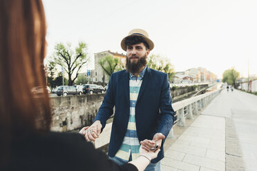 Over shoulder view of man holding girlfriend's hands by city canal - CUF12428