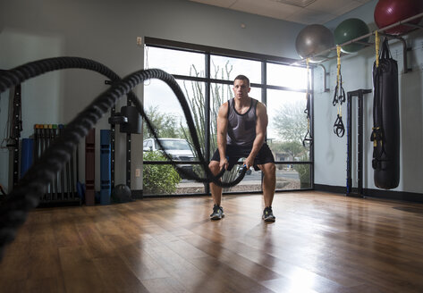 Mann trainiert mit Kampfseil im Fitnessstudio - CUF12429