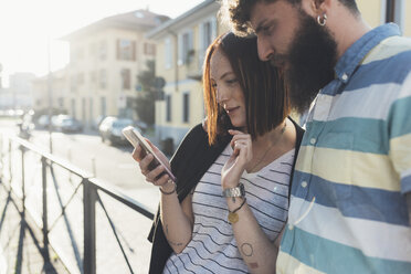 Pärchen auf dem Bürgersteig schaut auf das Smartphone - CUF12457