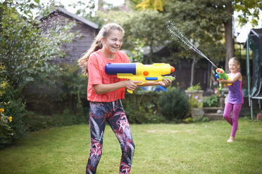 Teenager-Mädchen und ihre Schwester kämpfen mit einer Wasserpistole im Garten - CUF12463