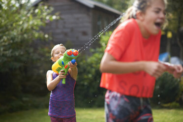 Junge bespritzt seine jugendlichen Schwestern mit Wasserpistole im Garten - CUF12466