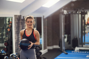 Junge Frau trainiert, hält Atlaskugel im Fitnessstudio - CUF12493