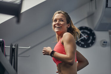 Junge Frau, die auf einem Laufband im Fitnessstudio trainiert und über ihre Schulter schaut - CUF12504