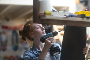 Woman working in skateboard shop, attaching wheels to skateboard - CUF12512