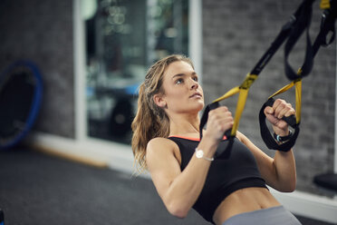 Junge Frau macht Klimmzüge an Übungsgriffen im Fitnessstudio - CUF12514