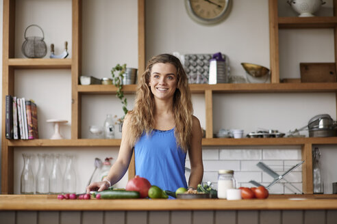 Glückliche junge Frau steht an der Küchentheke und bereitet Gemüse vor - CUF12525