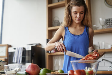 Young woman at kitchen table slicing tomatoes - CUF12528