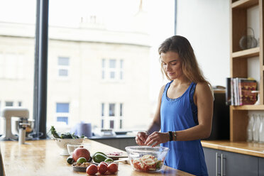 Junge Frau am Küchentisch bei der Zubereitung einer Salatschüssel - CUF12529