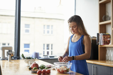 Young woman at kitchen table preparing salad bowl - CUF12529