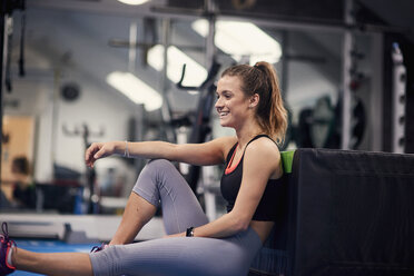 Happy young woman training, sitting on gym floor - CUF12539