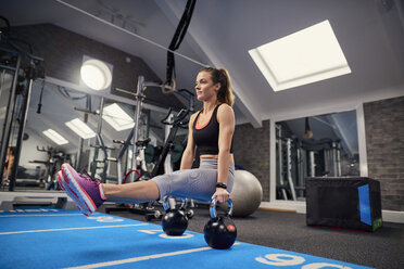 Junge Frau trainiert, macht Sit up Push ups auf Kettle Bells im Fitnessstudio - CUF12542