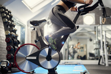 Neck down view of young woman training, pedalling exercise bike in gym - CUF12547