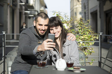 Junges Paar sitzt vor einem Café und macht ein Selfie mit seinem Smartphone - CUF12563