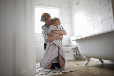 Mother and daughter in bathroom, mother wrapping daughter in bath towel, hugging her - CUF12578