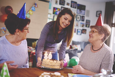 Daughter presenting birthday cake to mother at birthday party - CUF12580