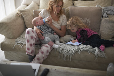 Mother feeding baby son and helping daughter with digital tablet - CUF12592