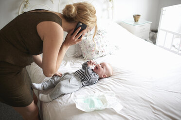 Mutter wechselt die Windel ihres kleinen Sohnes, während sie ein Mobiltelefon benutzt - CUF12593