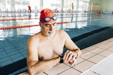 Älterer Mann, der am Rande eines Schwimmbeckens die Zeit im Wasser liest - CUF12612