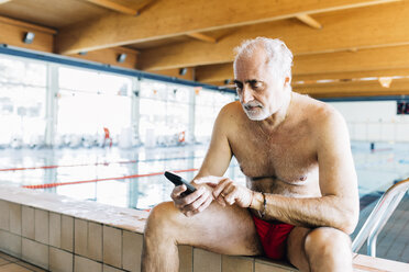Senior man using mobile phone by edge of swimming pool - CUF12621