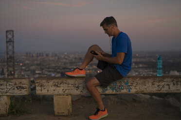 Jogger sitzt auf einer Bank und schaut auf sein Smartphone, Runyon Canyon, Los Angeles, Kalifornien, USA - ISF02111