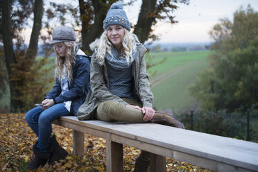 Porträt eines Mädchens und ihrer Schwester, die auf einer Parkbank im Herbst sitzen - CUF12877